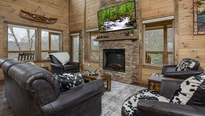 Ein gemütliches Blockhaus-Interieur mit Kamin aus Stein, Ledersofas und einem Wand-Fernseher.