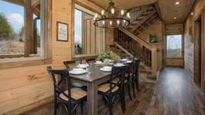Ein Essbereich mit Holzboden, einer Chandelüster, einer Treppe und großen Fenstern.