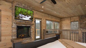 Ein Schlafzimmer mit Kamin aus Stein, einem an der Wand befestigten Fernseher und großen Fenstern.