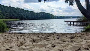 A sandy beach with a wooden pier extending into calm water, surrounded by dense greenery. - Vacation apartment in a cozy farmhouse by the bathing lake with large garden and sauna (Carpin)