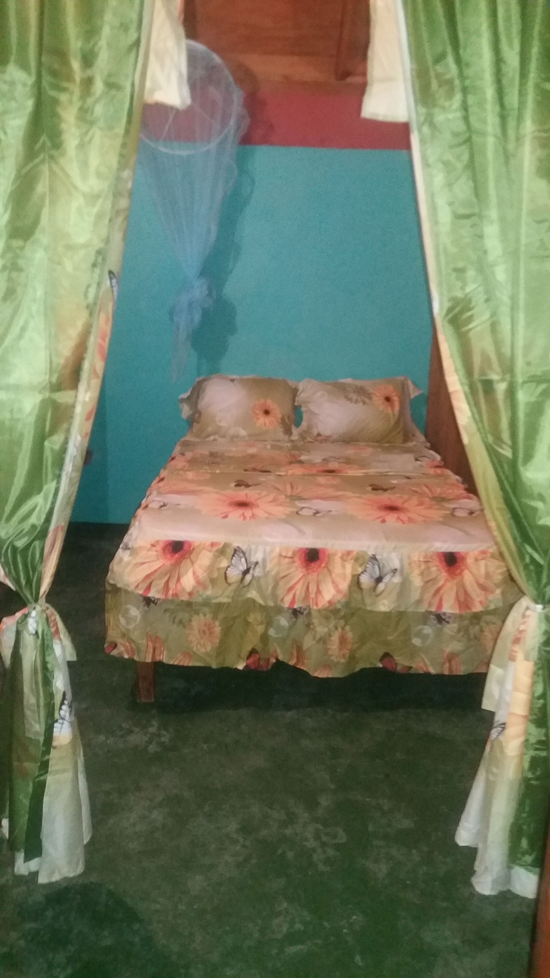 Een bed met bloemenbeddengoed en een klamboe in een kamer met een groene vloer en een blauwe muur.