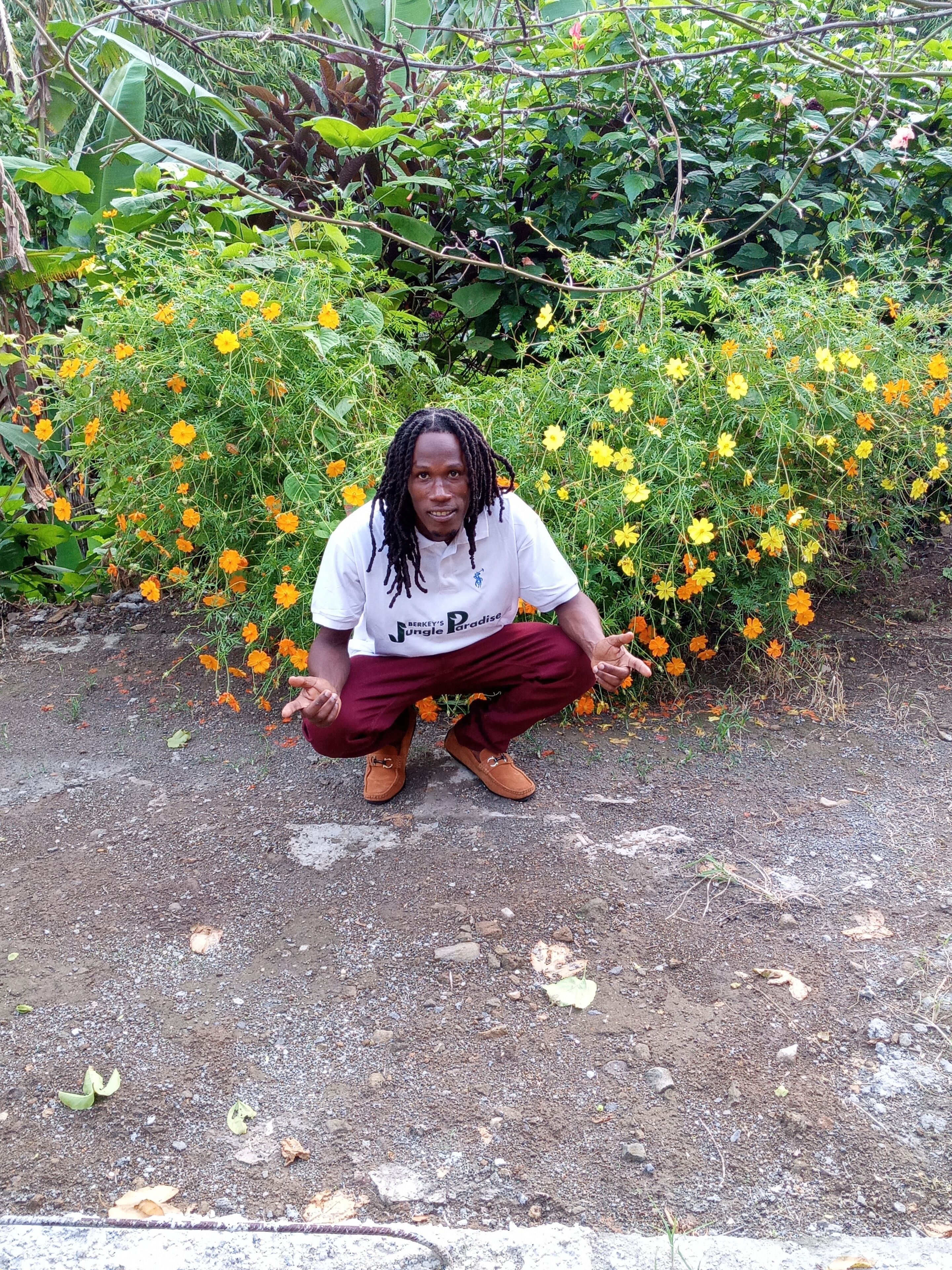 A person crouching in front of a garden with various plants and flowers.
