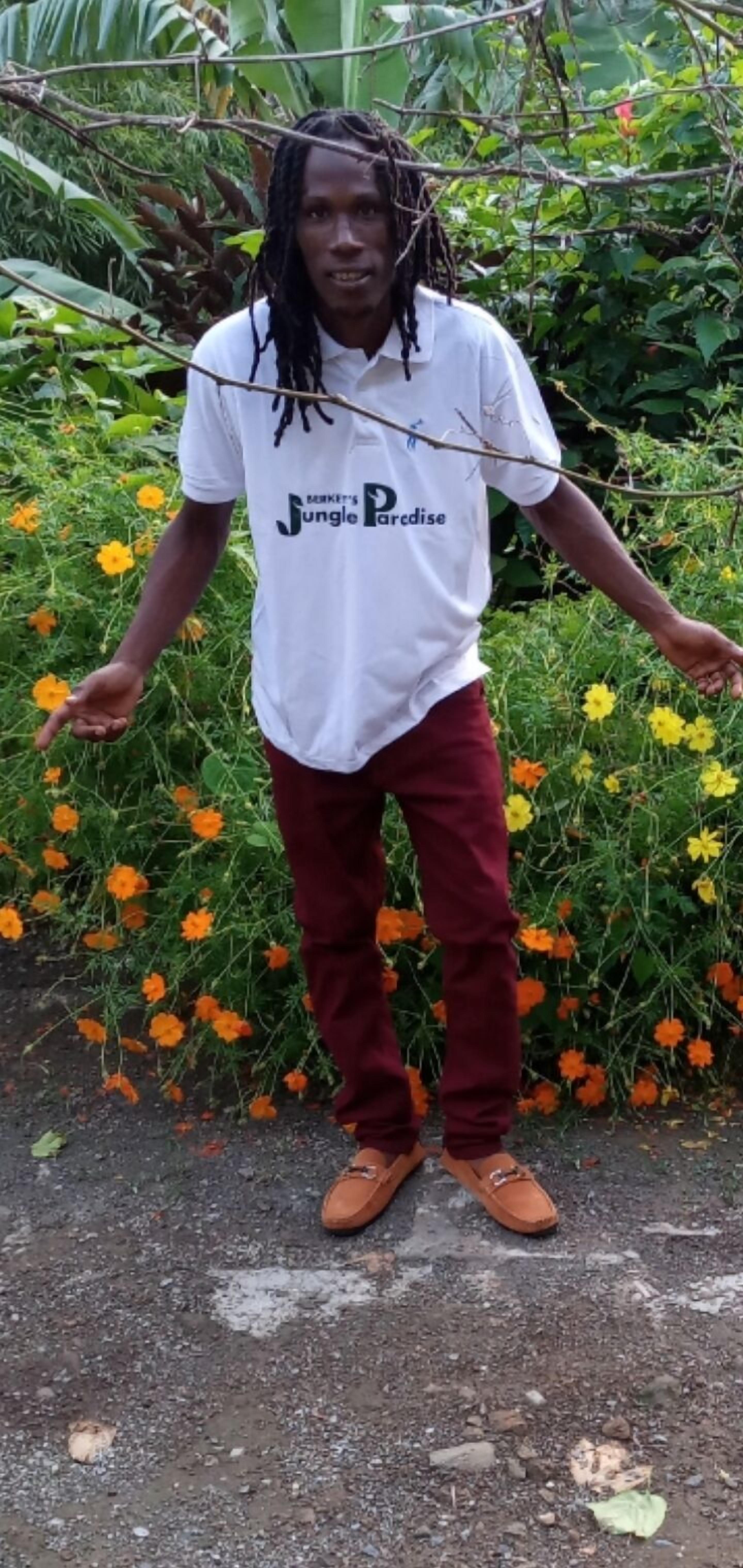A person standing in a garden with a white shirt and maroon pants.