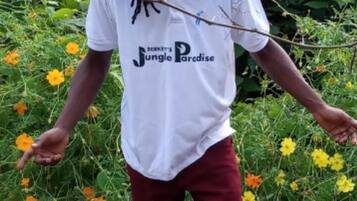 A person standing in a garden with a white shirt and maroon pants.