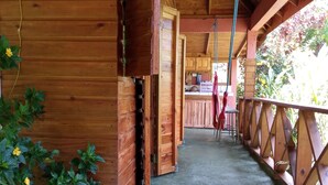 A wooden cabin with a porch, a concrete floor, and a view of the surrounding area. - Berkey's Jungle Paradise (Roseau)