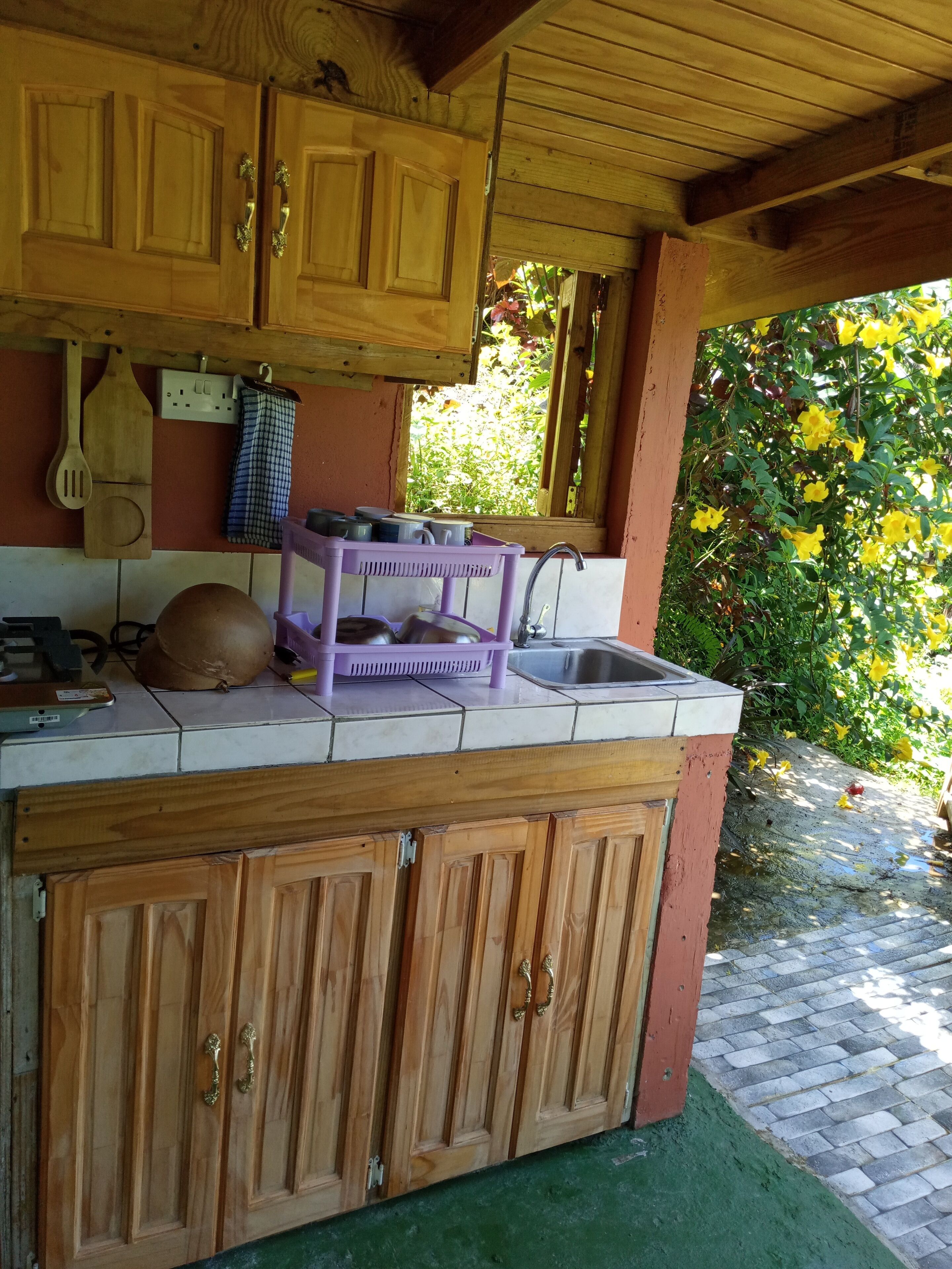 A rustic kitchen with wooden cabinets, a purple dish rack, and a window overlooking greenery.