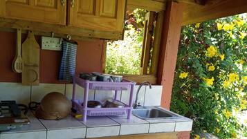 A rustic kitchen with wooden cabinets, a purple dish rack, and a window overlooking greenery.
