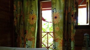 A room with a bed covered in floral-patterned bedding, curtains with floral and butterfly designs, and a window with a view of greenery outside. - Berkey's Jungle Paradise (Roseau)