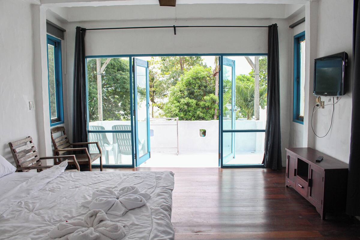 A bedroom with a bed, a wooden chair, a TV, and a sliding glass door leading to an outdoor area.