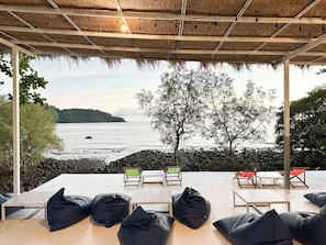 A beachside seating area with a view of the sea, a thatched roof, and a tree in the background. - Capital O 75411 Navagio​ Boutique​ Koh​ Chang (Prachuap Khiri Khan)