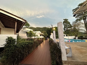 A pathway leading to a pool area with a wooden deck and white buildings. - Capital O 75411 Navagio​ Boutique​ Koh​ Chang (Prachuap Khiri Khan)