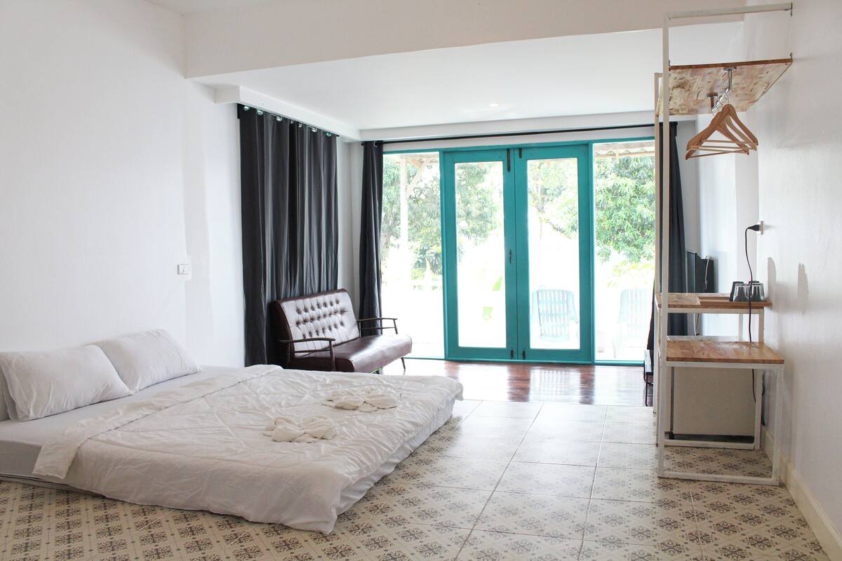 A bedroom with a bed, a bench, a hanging rack, and a view of the outdoors.