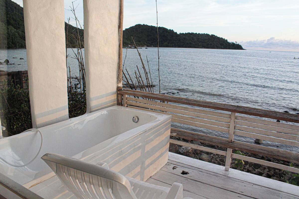 A wooden deck with a hot tub and a view of a calm lake and distant hills.