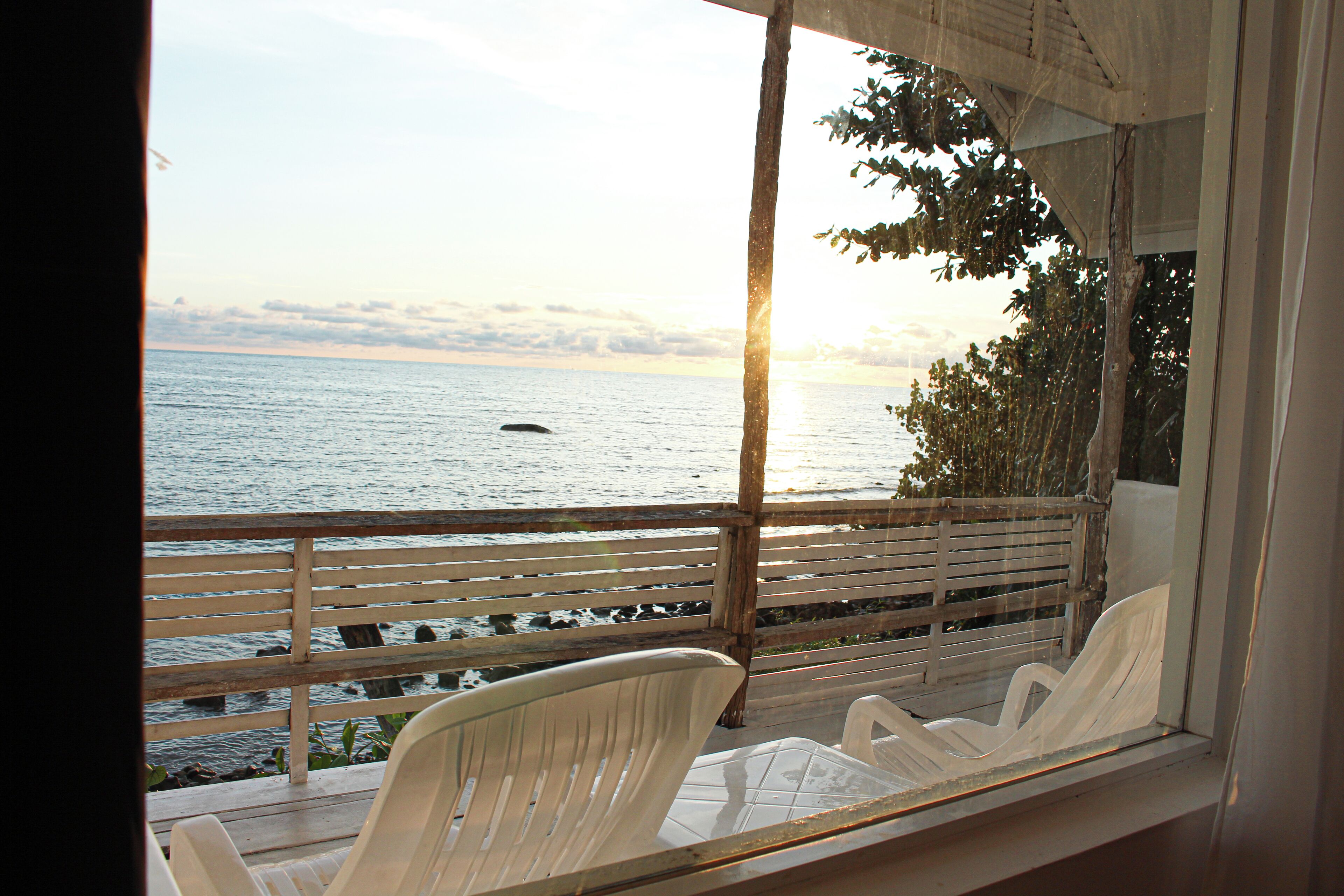 A balcony with a view of the sea, wooden railing, and two white plastic chairs.