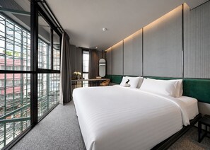 Une chambre d’hôtel moderne dotée d’un grand lit, d’un bureau et offrant une vue sur la ville grâce à de grandes fenêtres du sol au plafond.