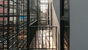 A narrow corridor with metal railings and a wooden floor, leading to a balcony with a view of the cityscape. -  Goose Living Bangkok BTS Phra Khanong (Bangkok)