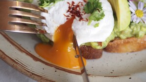 Un plato de desayuno con aguacate, huevo pochado y cilantro sobre tostada.