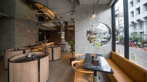 A modern cafe with round tables and booths, a large window with a view of the street, and a circular skylight. -  Goose Living Bangkok BTS Phra Khanong (Bangkok)