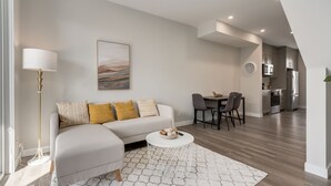 A modern living room with a sofa, a coffee table, and a dining area with chairs. - *MODERN* 2BDRM Close to Airport & Major Highway (Calgary)