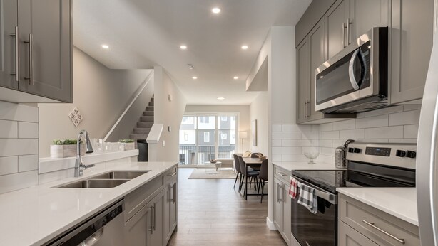 A modern kitchen with stainless steel appliances, a dishwasher, and a dining area with a table and chairs. - *MODERN* 2BDRM Close to Airport & Major Highway (Calgary)