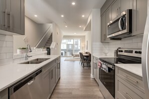 A modern kitchen with stainless steel appliances, a dishwasher, and a dining area with a table and chairs. - *MODERN* 2BDRM Close to Airport & Major Highway (Calgary)