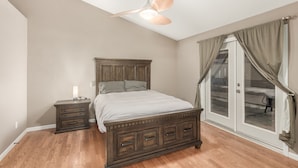 Un dormitorio con cama de madera, mesita de noche, ventilador de techo y puerta corrediza de vidrio con cortinas.