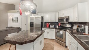 Una cocina moderna con gabinetes blancos, electrodomésticos de acero inoxidable, encimera de granito y una lámpara colgante.