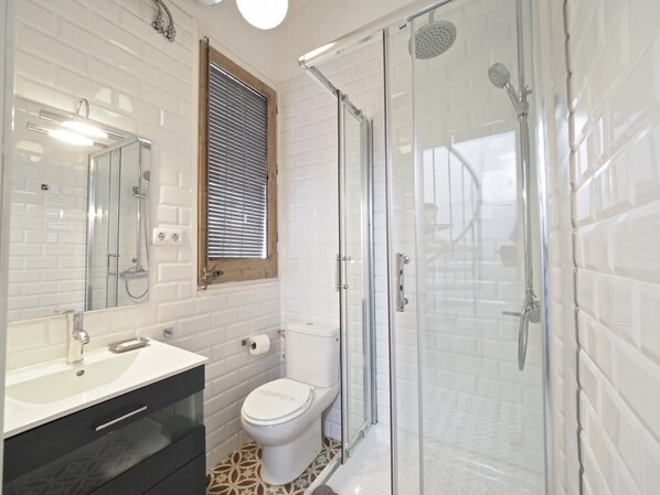A modern bathroom with a glass-enclosed shower, a white toilet, and a sink with a mirror above it. - Sunny Rooftop Apartment (Barcelona)