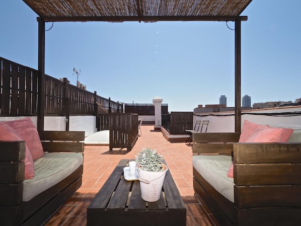 A rooftop terrace with wooden furniture, a pergola, and a view of the city skyline.