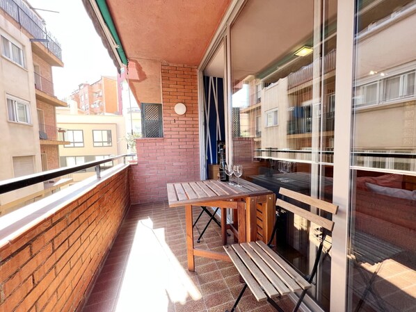 Een balkon met een houten tafel en stoelen, een bakstenen muur en een glazen deur die leidt naar een binnenruimte.