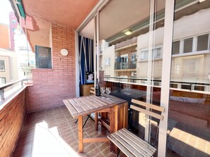 Een balkon met een houten tafel en bank, een televisie en een fles champagne.