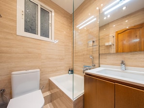 Une salle de bain moderne avec une douche à parois de verre, des toilettes blanches et un meuble-lavabo en bois avec un miroir.