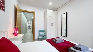 Una habitación de hotel con una cama, un cojín rojo, una silla azul, un espejo y un armario.