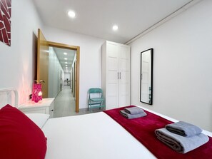 Une chambre d’hôtel avec un lit, un oreiller rouge, une chaise bleue, un miroir et une armoire.