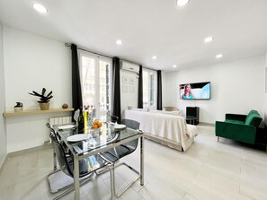 Un salon moderne avec une table à manger en verre, un canapé et un téléviseur fixé au mur.