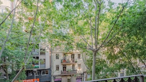 Un balcón con barandilla de hierro forjado que da a una calle con edificios y árboles.