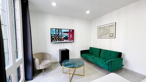 Una sala moderna con un sofá verde, una mesa redonda, un sillón beige, un televisor montado en la pared y un mapa enmarcado.