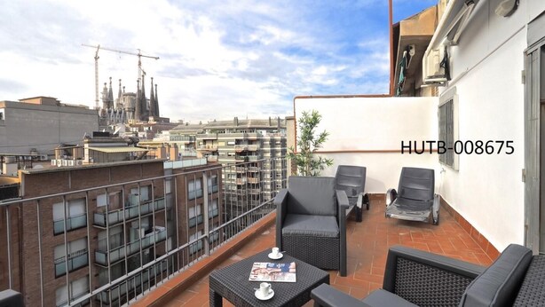 A rooftop terrace with outdoor seating, a view of the cityscape, and a construction crane in the background. - Sagrada Familia Penthouse (Barcelona)
