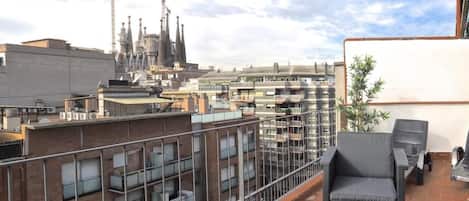 Una terraza en la azotea con mobiliario exterior, vistas de la ciudad y una grúa de construcción al fondo.