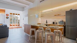 Een moderne keuken met een centraal eiland, witte barkrukken, een ingebouwde magnetron en een roestvrijstalen koelkast.
