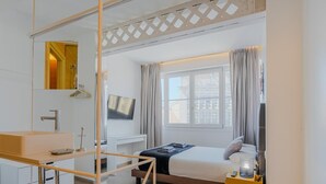 Een moderne hotelkamer met een bed, nachtkastje, televisie en een raam met gordijnen.