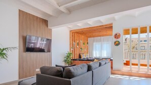 Een moderne woonkamer met een hoekbank, een flatscreen televisie, houten lambrisering en uitzicht op buiten.