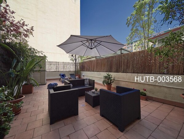 An outdoor patio with a seating area, a large umbrella, and potted plants. - Gran Via Terrace Barcelona (Barcelona)