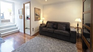 Ein Wohnzimmer mit grauem Sofa, zwei Beistelltischen mit Lampen, einem gemusterten Teppich und einem gerahmten Bild an der Wand.