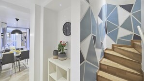 Ein modernes Interieur mit Essbereich, einer Uhr und einer Treppe mit geometrischem Wanddesign.