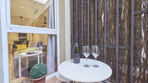 Ein kleiner Tisch im Freien mit einer Weinflasche und zwei Gläsern, einem Blumentopf und Blick auf den Innenraum eines Gebäudes durch eine Glastür.