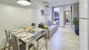 Ein modernes Wohnzimmer mit Essbereich, einem grauen Sofa, einem Glastisch und einem großen Fenster.
