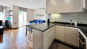 Et moderne køkken med en central ø, integrerede hårde hvidevarer og et spiseområde med en blå sofa.