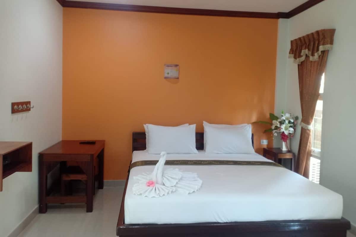 A hotel room with a bed, a nightstand, a wooden side table, and a window with curtains.