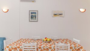 A dining area with a table set for four, featuring a fruit centerpiece, white chairs, and wall-mounted artwork. - La Dimora Di Montelittu With AC (Loiri Porto San Paolo)